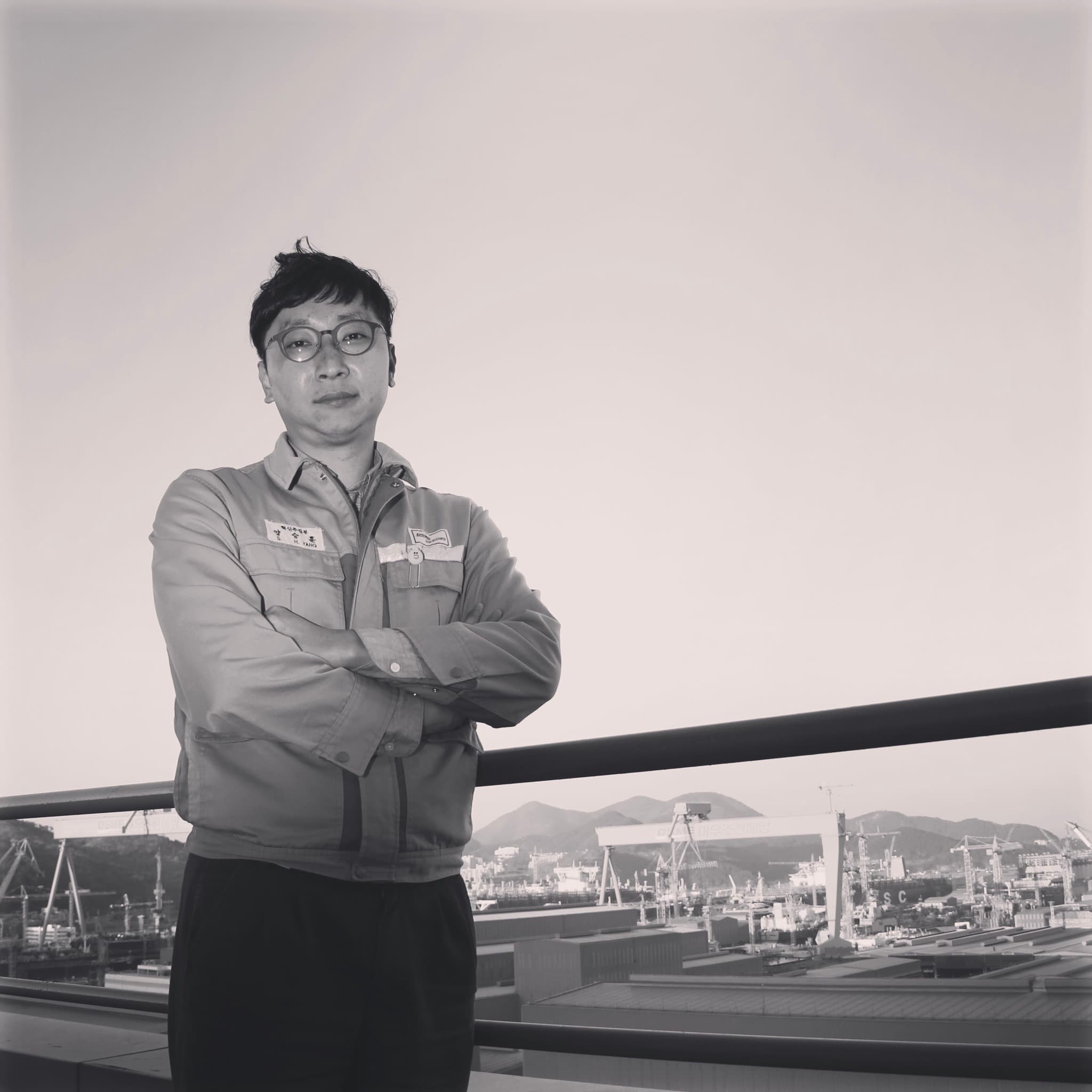 Seunghoon Yang in workwear overlooking the shipyard